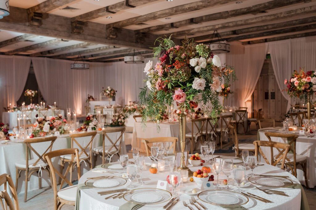  wedding reception dinner is set up in a ballroom at rancho bernardo inn. the decor is white, pinks, greens, reds with gold accents and light wood