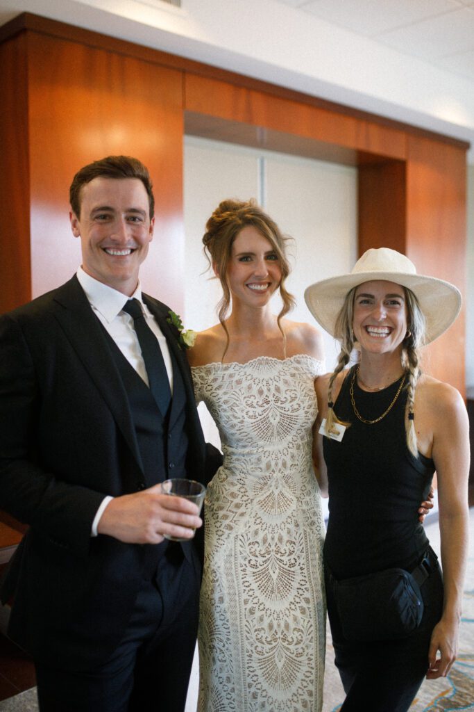 the image depicts the bride and groom standing with their wedding planner from sweet blossom weddings. they are standing and smiling together for a photo, with their arms around each other 