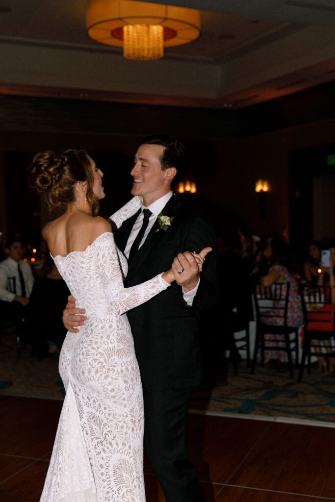 the bride and groom are slow dancing together on the dance floors, sharing their first dance as husband and wife. they are smiling at each other. 