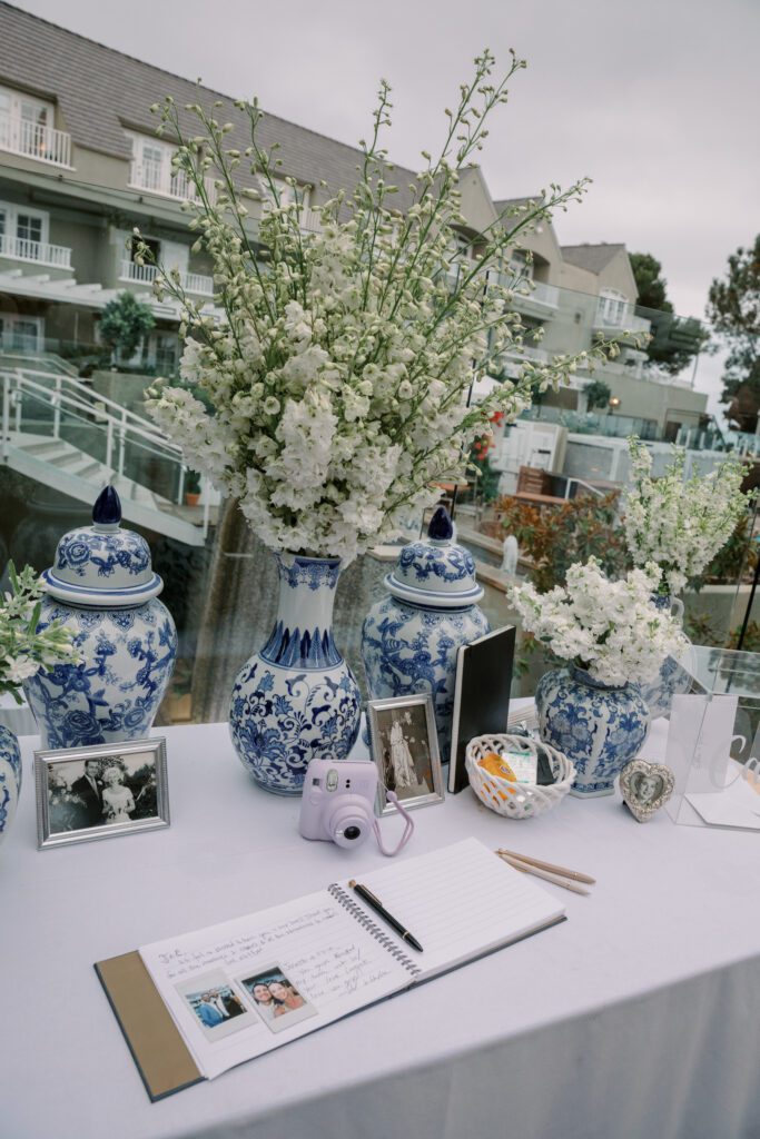 showing the details of the blue and white decorative vases holding the florals at the cocktail hour. multiple vases on a white linen table and the guest book in front.creating a coastal and timeless theme