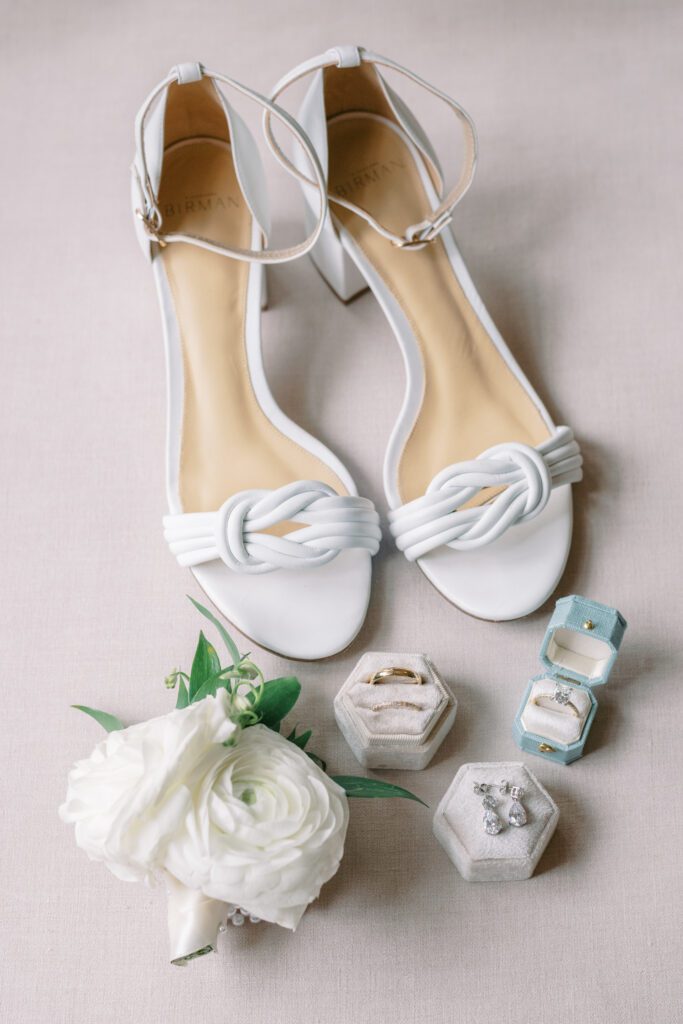 depicts details of getting ready before a wedding, including the brides white heel shoes and white flowers with 3 ring boxes holding the jewelry for the wedding.
