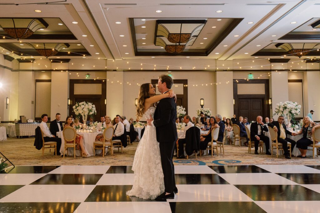 bride and groom are sharing their first dance at their wedding. they are inside a ballroom at rancho bernardo inn and dancing on a black and white checkered dance floor