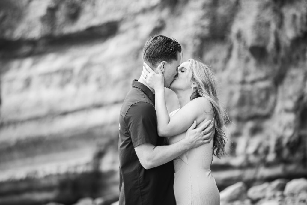 Newly engaged couple at the beach holding each other and kissing 