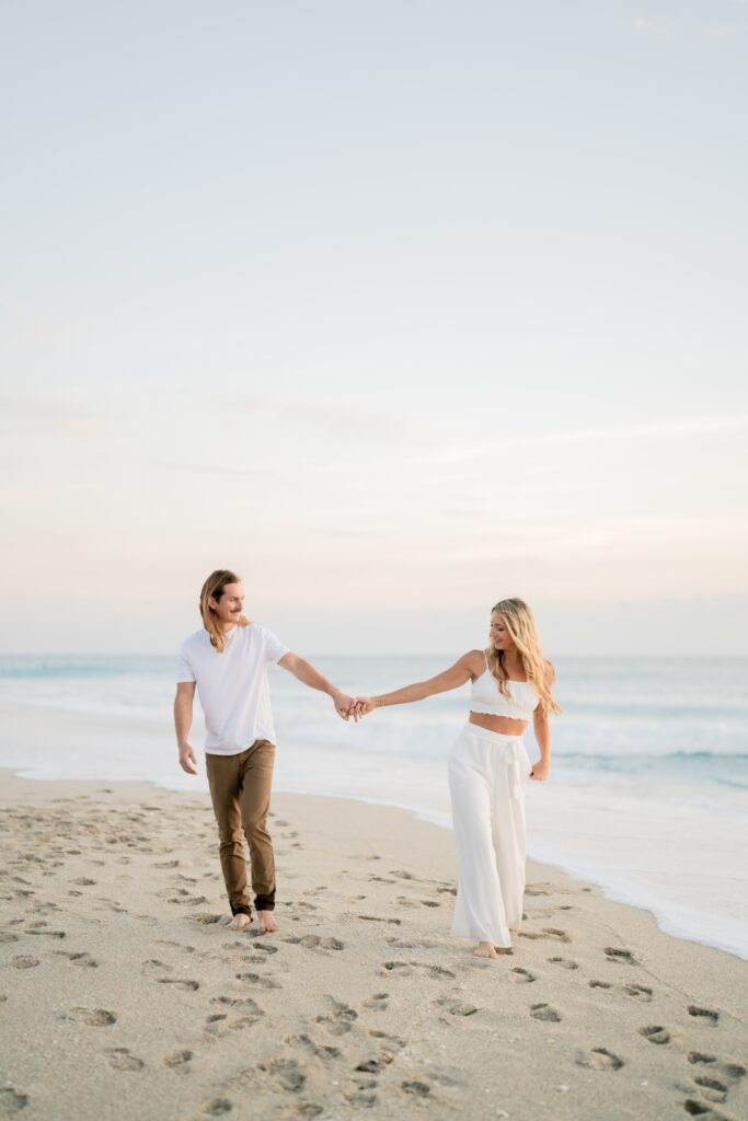 Newly engaged couple at the beach holding hands and demonstrating our engagement photo tips and styling advice
