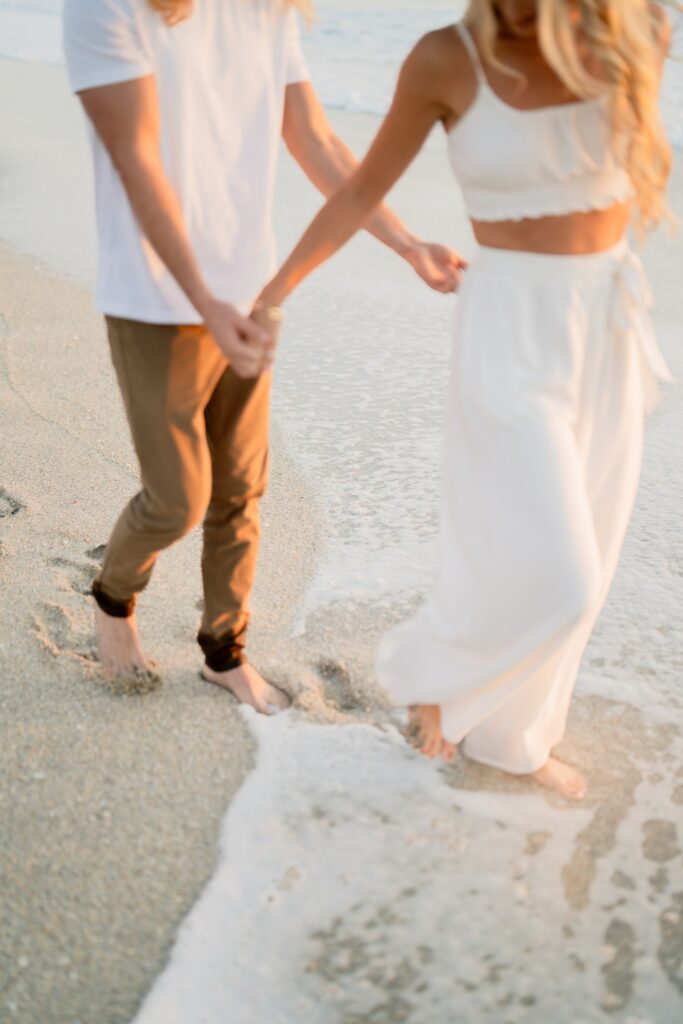Newly engaged couple at the beach holding hands 
