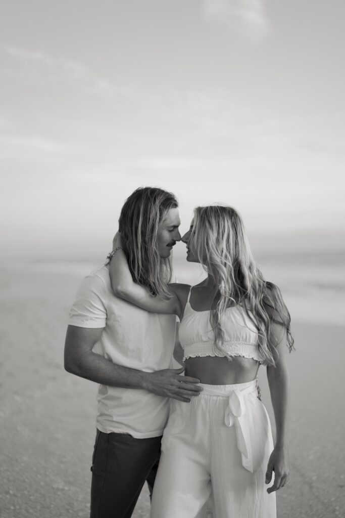 Newly engaged couple at the beach holding each other and kissing in black and white
