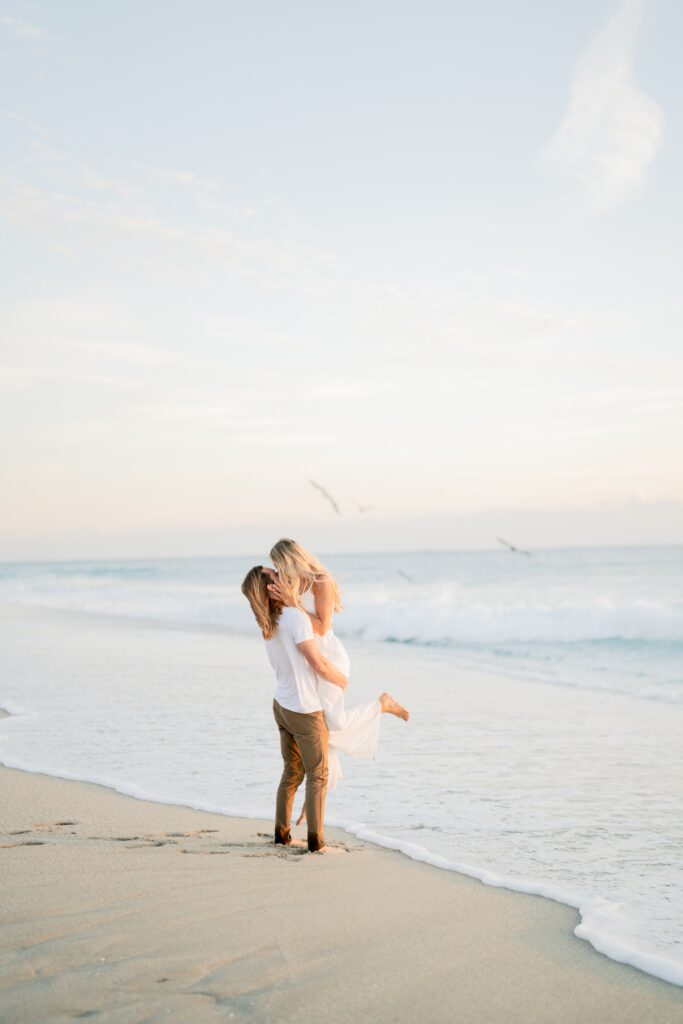 Newly engaged couple at the beach holding each other and kissing and demonstrating our engagement photo tips and styling advice