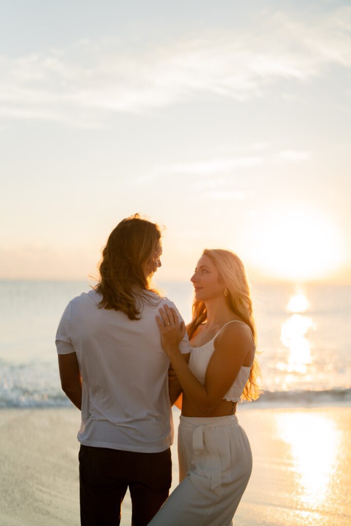 Newly engaged couple at the beach looking at each other during sunset
